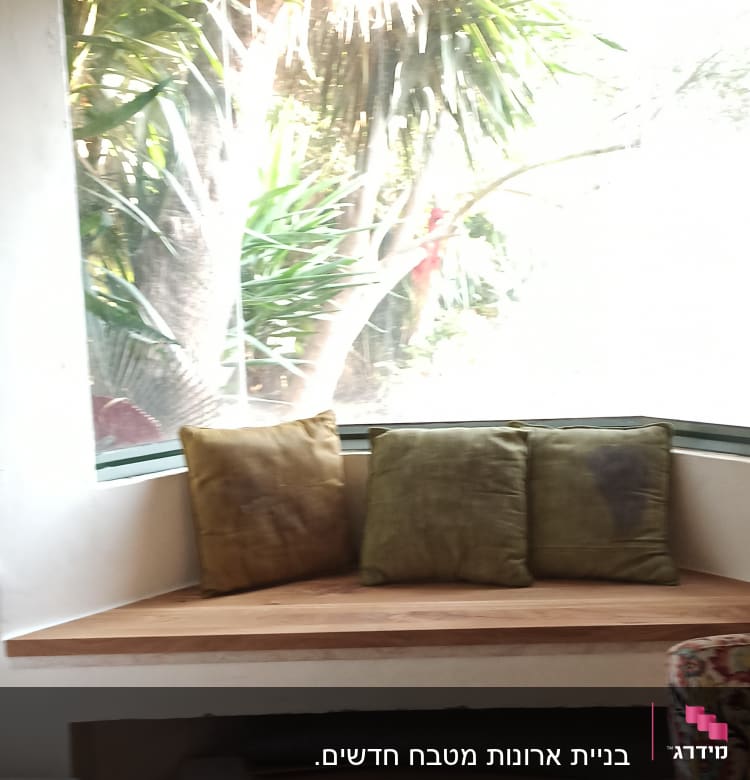 כריות על ספסל עץ ליד חלון גדול עם נוף לצמחייה